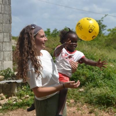 Projects Abroad Kinderopvang vrijwilliger in Jamaica gooit een bal naar een kind om de hand-oog coordinatie te verbeteren. Een vrijwilligers werkt met kinderen in Jamaica en doet een buitenactiviteit om de hand-oog coordinatie te verbeteren tijdens het Kinderopvang project.
